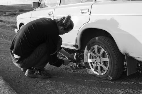 A person fixing a flat tire along the road